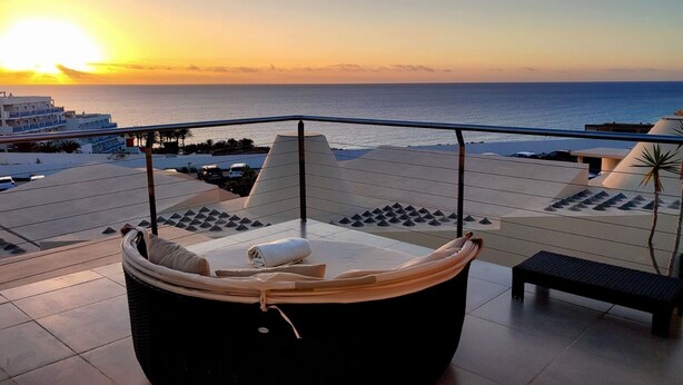 A balcony with a cushioned seating area and a view of the sunset over the sea. - FuerteVillage (Pajara)