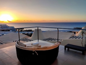 A balcony with a cushioned seating area and a view of the sunset over the sea. - FuerteVillage (Pajara)