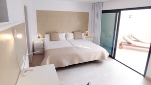 A modern hotel room with a large bed, a desk, and a balcony with a sun lounger. - FuerteVillage (Pajara)