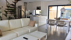 A modern living room with a white sofa, a coffee table, and a dining area with chairs and a table. - FuerteVillage (Pajara)