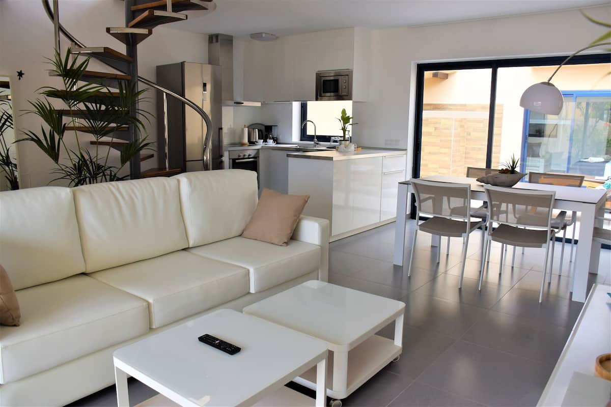 A modern living room with a white sofa, a coffee table, and a dining area with chairs and a table.