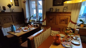 A cozy dining area with wooden furniture, a table set for breakfast, and a view of the street through a window. - Landhaus Grassmann (Piding)