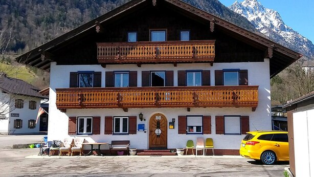 A two-story building with a balcony, a wooden door, and a mountain backdrop. - Landhaus Grassmann (Piding)
