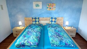 A double bed with blue bedding, two bedside tables with lamps, and a small table with towels. - Landhaus Grassmann (Piding)
