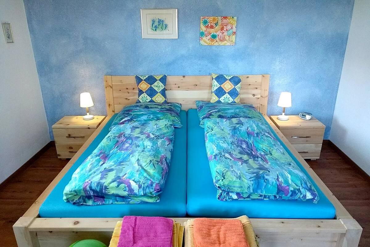 A double bed with blue bedding, two bedside tables with lamps, and a small table with towels.