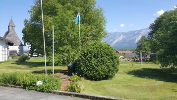 Une zone herbeuse avec un mât de drapeau, un petit bâtiment et une montagne en arrière-plan.