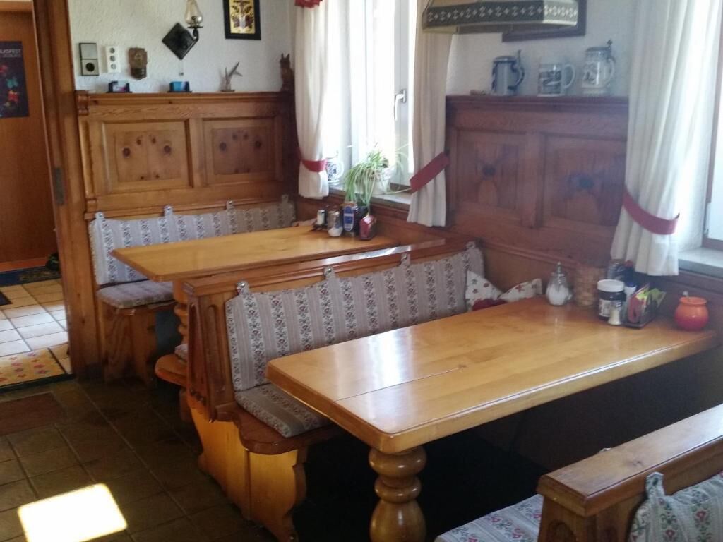 Ein traditioneller Essbereich aus Holz mit Bänken und einem Tisch, mit Heizkörper, Pflanze und verschiedenen Küchenutensilien auf der Fensterbank.