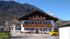 A two-story building with a balcony, a car parked in front, and a mountain in the background. - Landhaus Grassmann (Piding)