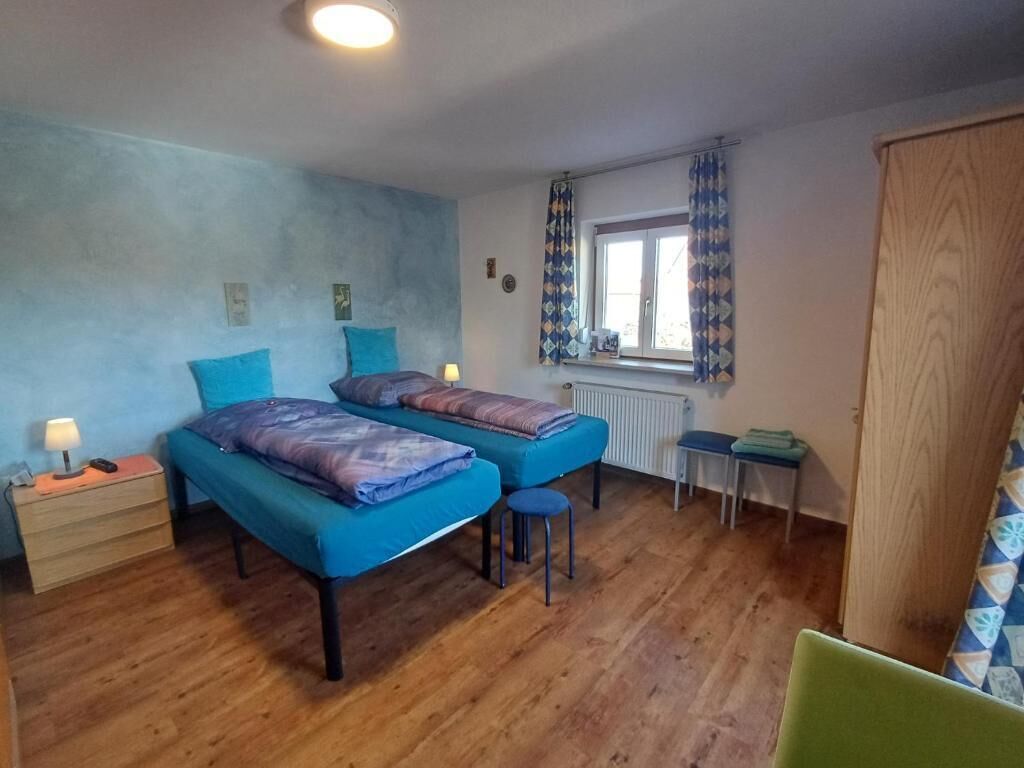 A bedroom with two beds, a wooden floor, a window with curtains, a radiator, and a small table.