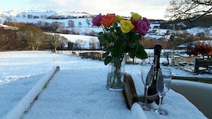 Eine verschneite Winterlandschaft mit einem Tisch, auf dem eine Vase mit bunten Rosen, eine Flasche Monetto Prosecco und zwei Weingläser stehen.