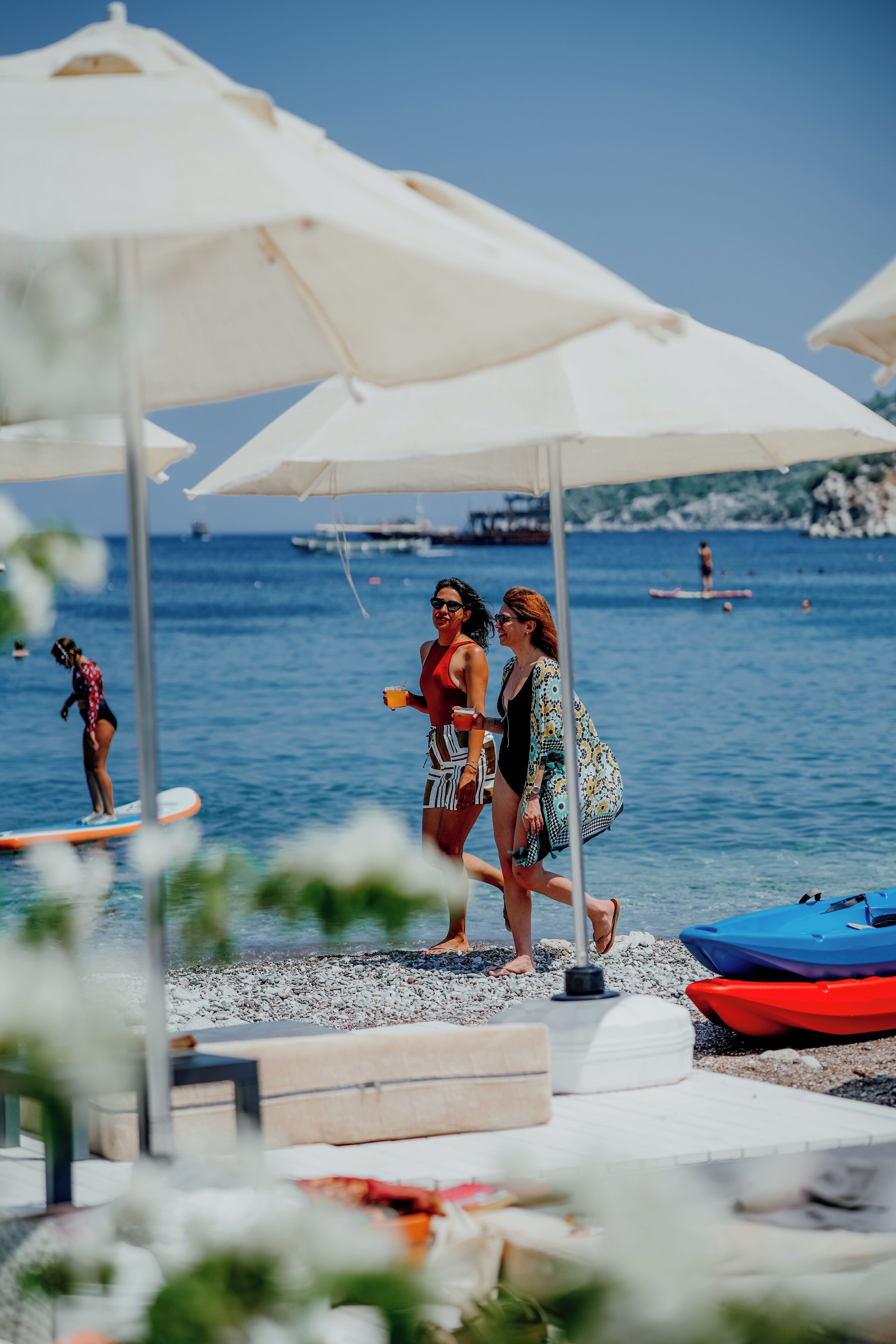 A beachside setting with umbrellas, a paddleboarder, and a row of boats.