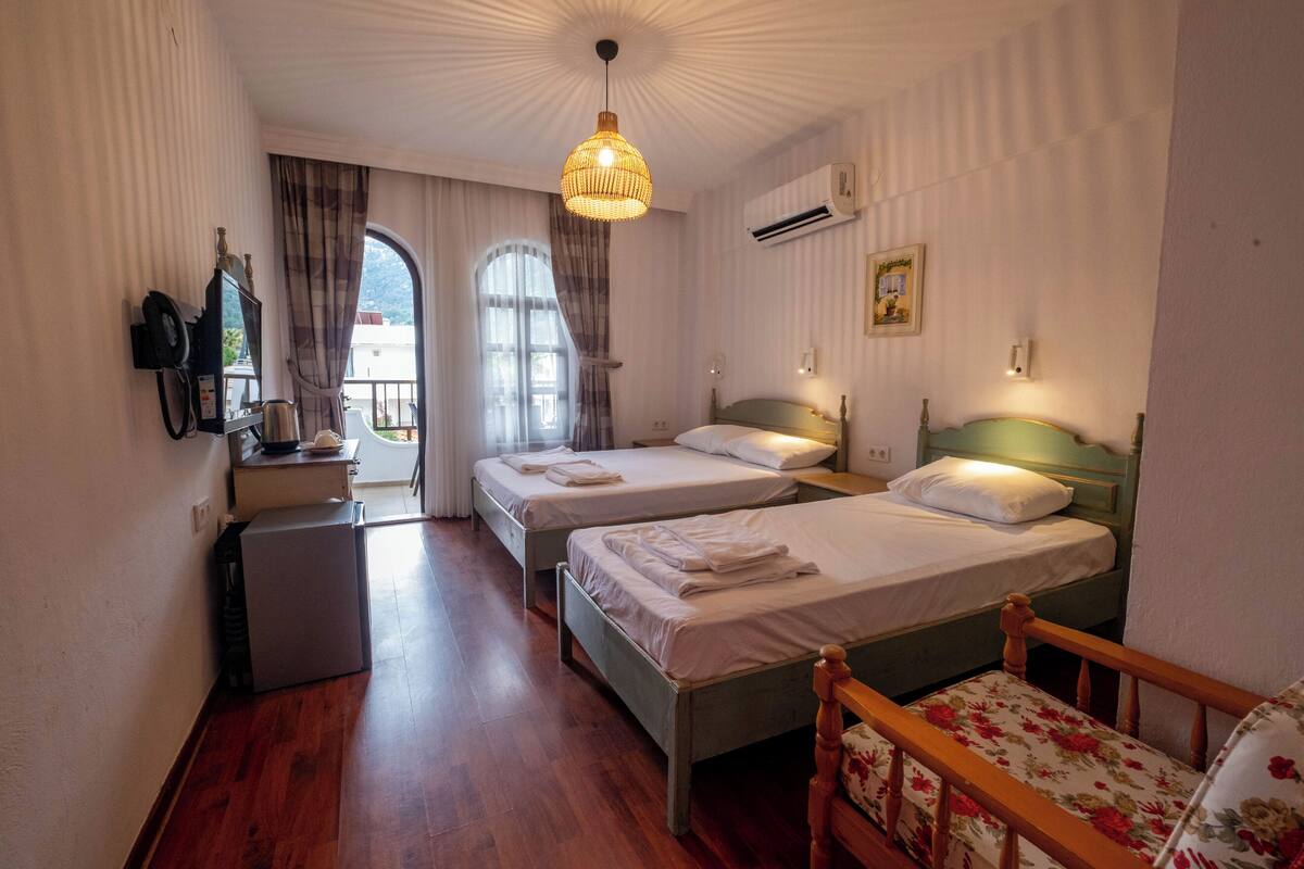 Une chambre d’hôtel avec deux lits, une petite kitchenette, un plancher en bois et une grande fenêtre avec des rideaux.