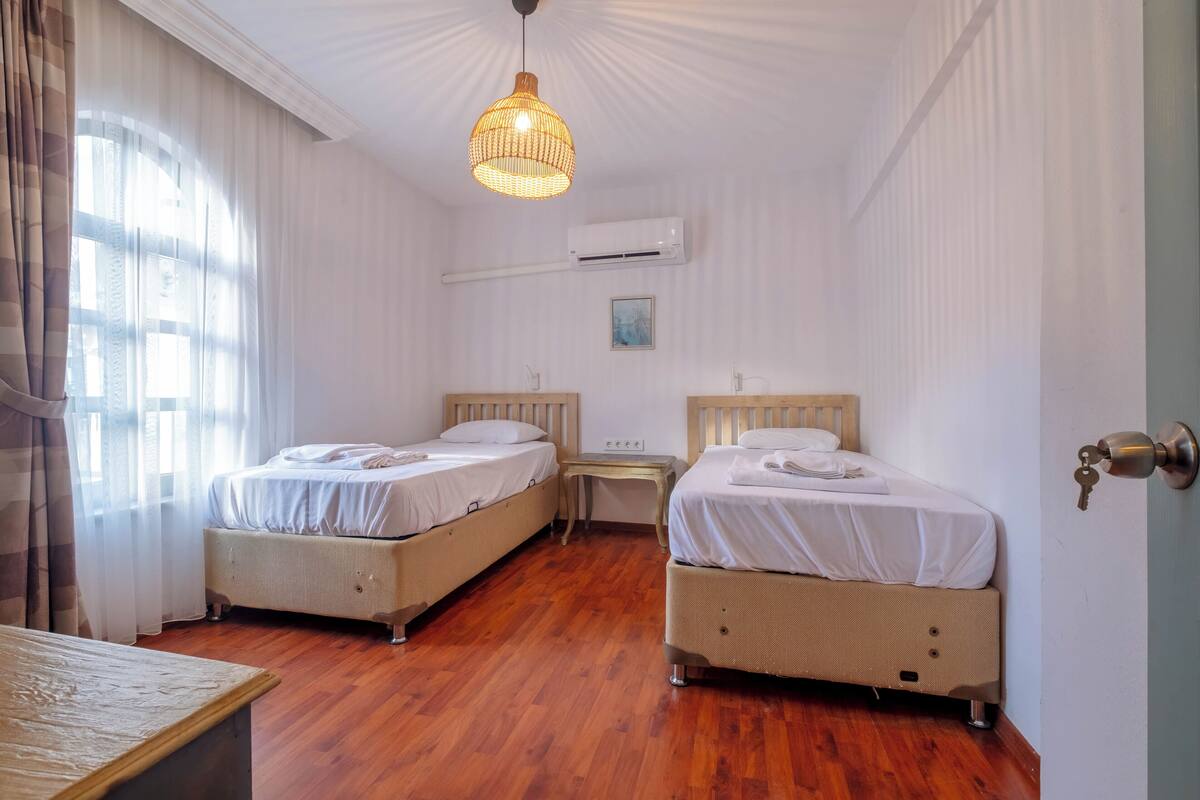 Une chambre avec deux lits, un plancher en bois, un luminaire suspendu, un appareil de climatisation et une porte à serrure.