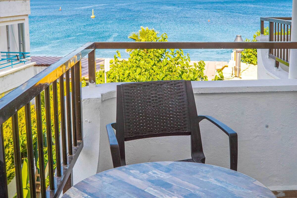 Un balcon avec une table ronde et une chaise, offrant une vue sur la côte et les montagnes qui se dessinent à l’horizon.