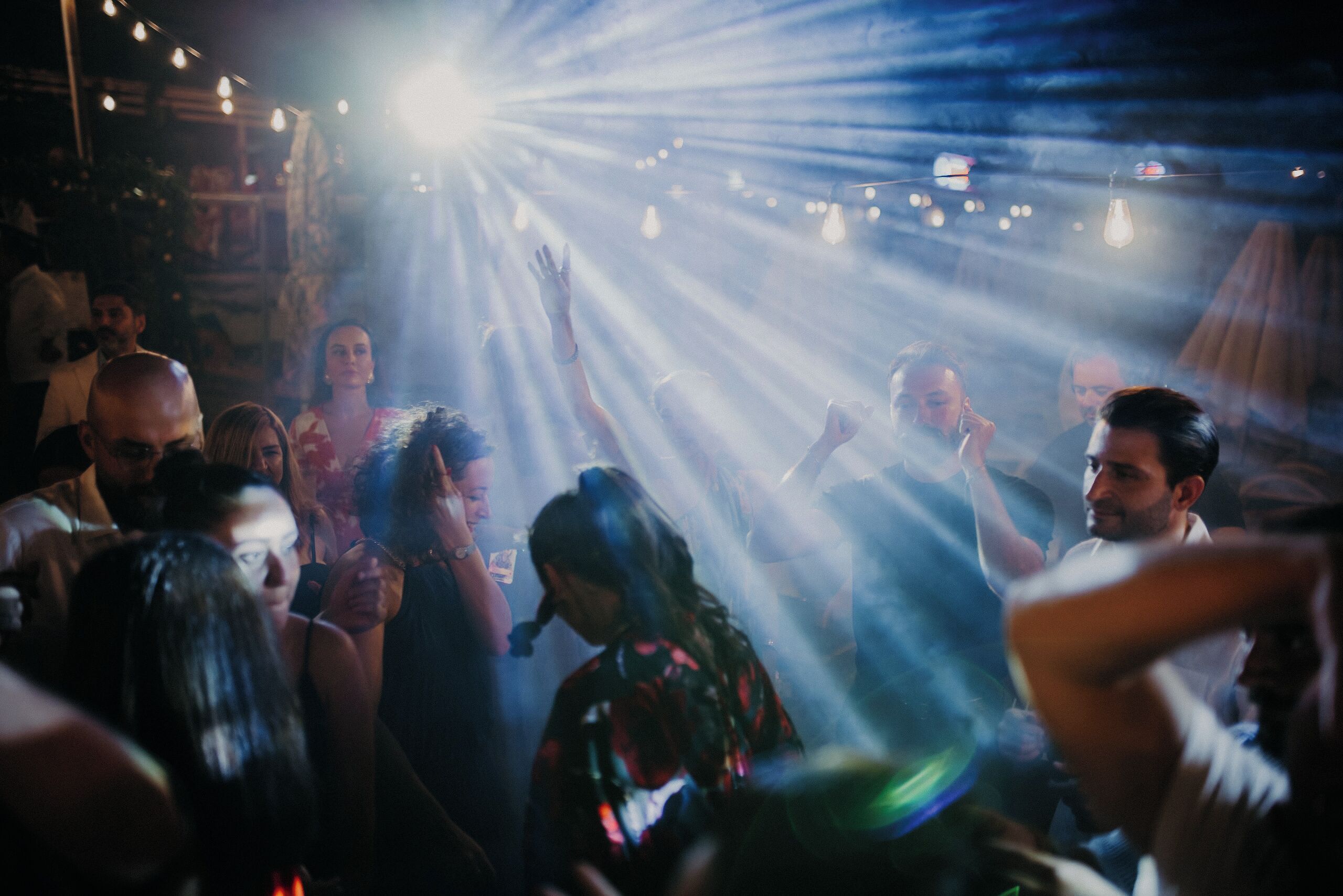 Een druk binnen evenement met dansende mensen en opgetrokken handen, onder fel licht.