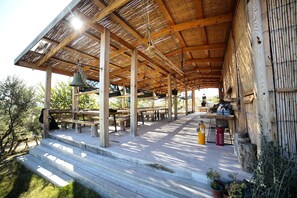 A wooden pavilion with a thatched roof, outdoor seating, and a fire extinguisher on the ground. - Vadi Alacati (Cesme)
