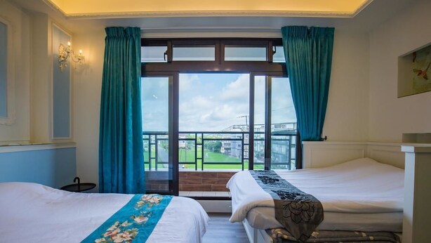 A hotel room with two beds, a large window with curtains, a view of a bridge, and a chandelier. - Yanduo Homestay (Luodong)