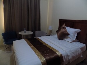 Una habitación de hotel con una cama, una silla, una mesita redonda y una lámpara.