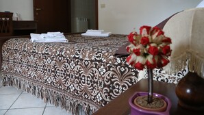 A neatly made bed with a patterned bedspread, a vase with red flowers, and a wooden side table with a vase. - B&B Severini (Morrovalle)
