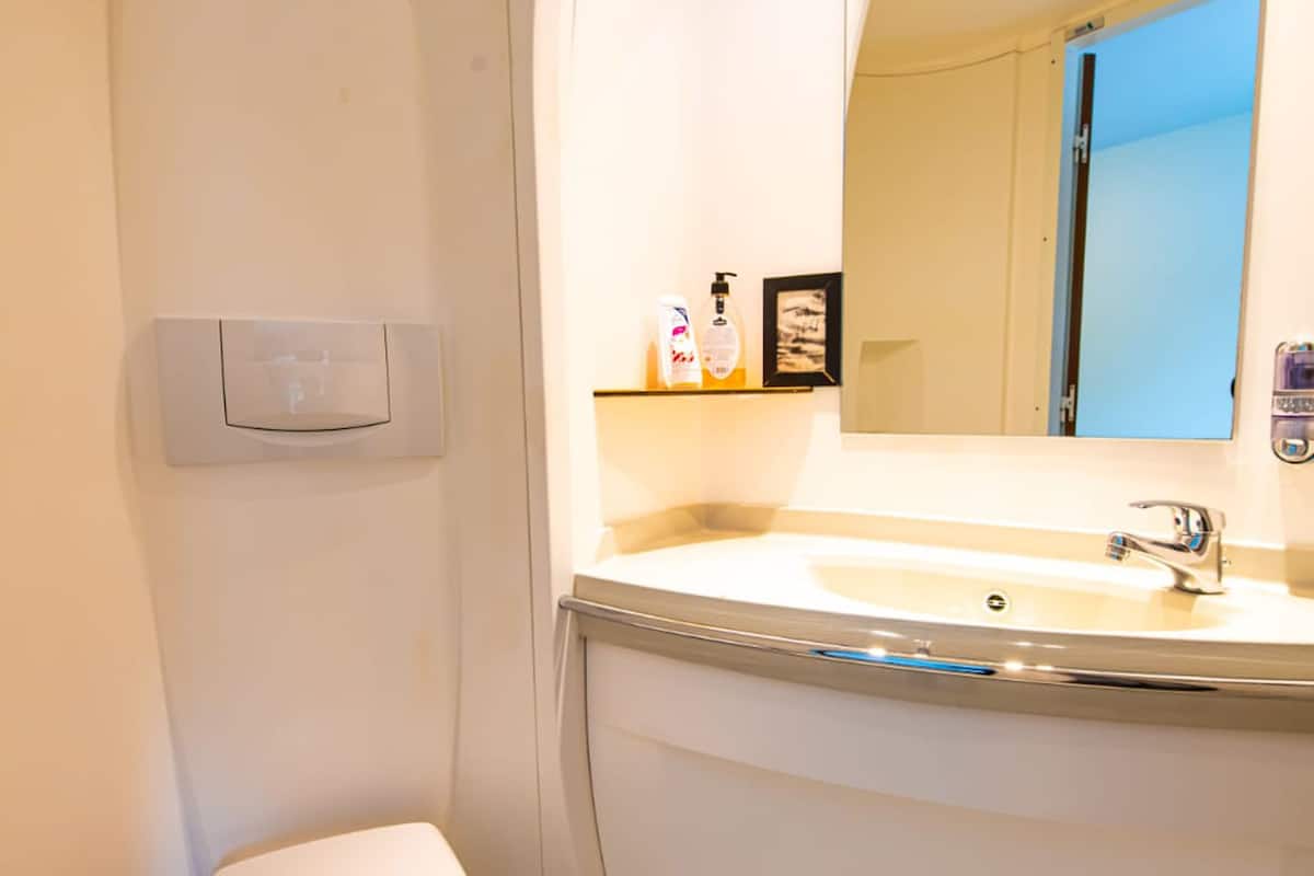 A bathroom with a toilet, sink, mirror, and a light switch on the wall.