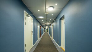 A long, narrow hallway with blue walls and white doors, carpeted floor, and overhead lighting. - Hotell Kvarntorget (Uppsala)