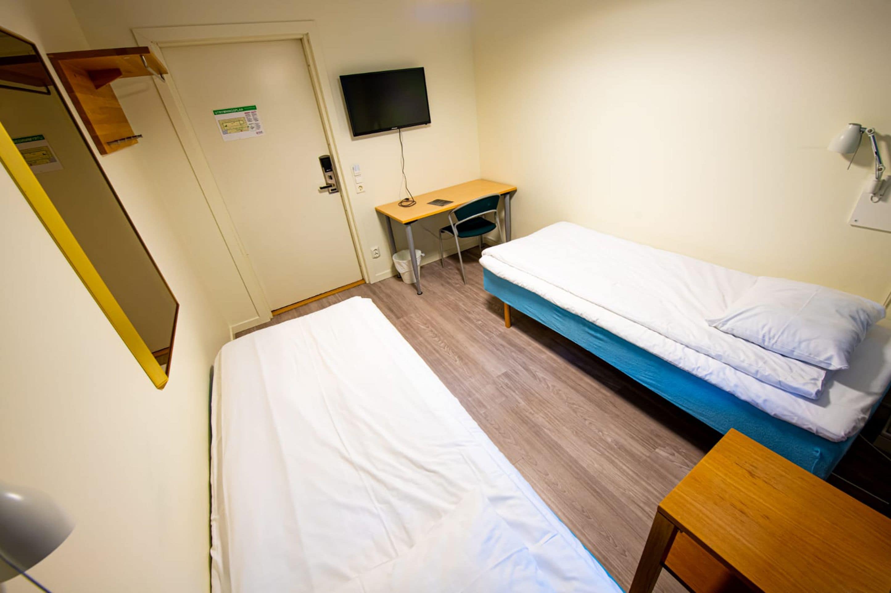 A room with two beds, a desk, a chair, a TV, and a door.