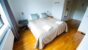 A bedroom with a bed, bedside tables, a nightstand, a radiator, and a window with curtains. - Hotell Kvarntorget (Uppsala)