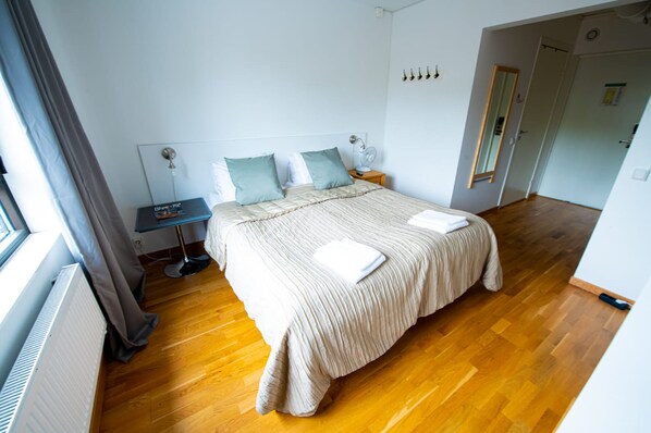 A bedroom with a bed, bedside tables, a nightstand, a radiator, and a window with curtains.