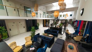A spacious lobby with multiple seating areas, including sofas and armchairs, a coffee table, and a dining area with a table and chairs. There are potted plants and a staircase leading to an upper level. - Hotell Kvarntorget (Uppsala)