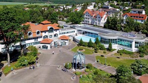 An aerial view of a modern building with a swimming pool, surrounded by greenery and residential houses. - Deluxe Double Room - Göbel's Hotel Aqua Vita (Bad Wildungen)