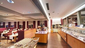 A buffet setup with various food items, a seating area with tables and chairs, and a counter with a display. - Deluxe Double Room - Göbel's Hotel Aqua Vita (Bad Wildungen)