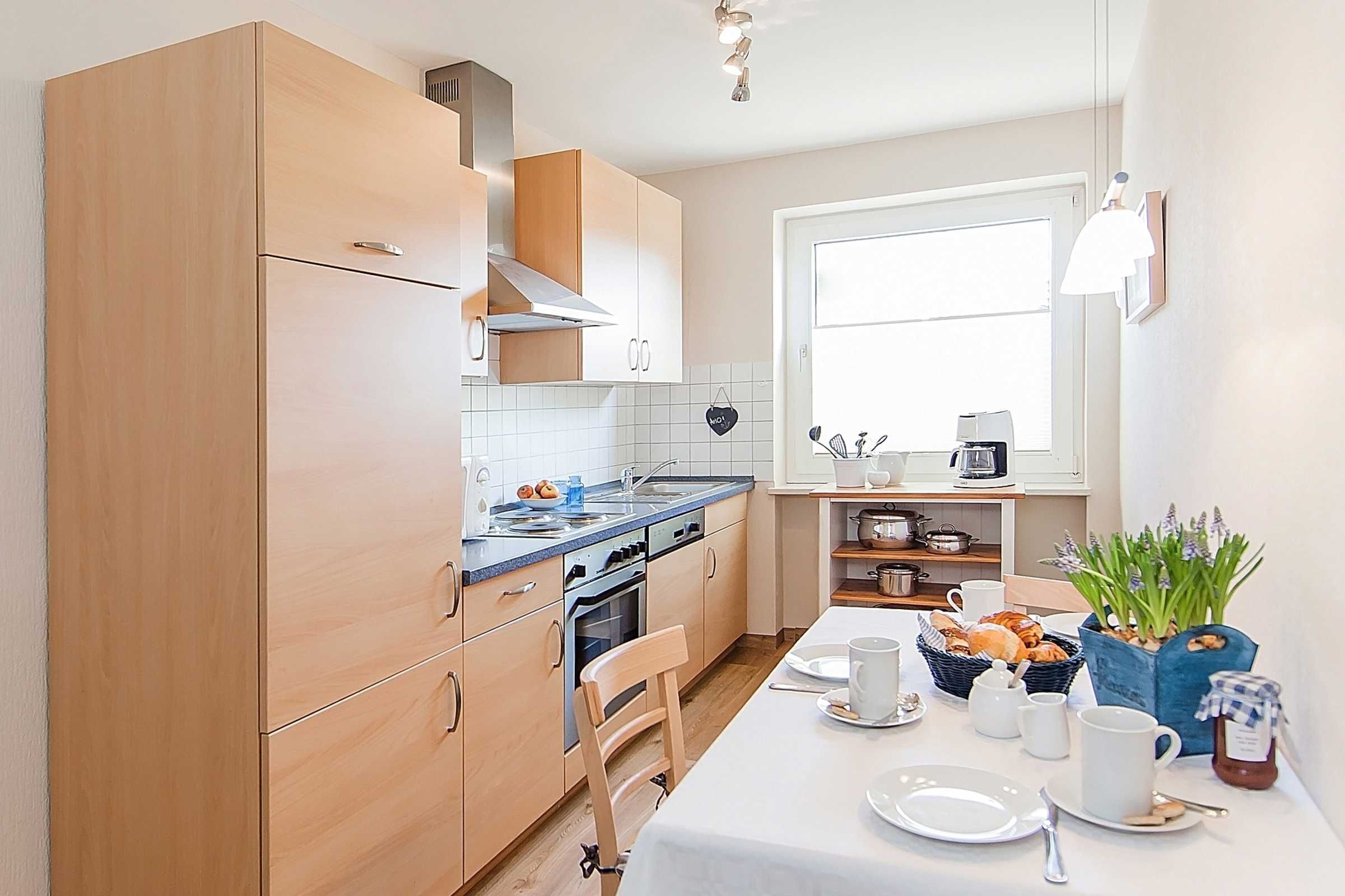 Una cocina moderna con armarios de madera, horno integrado y un comedor con mesa dispuesta para el desayuno.