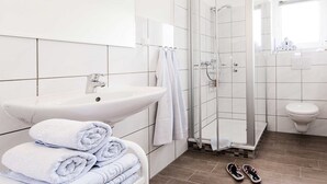 Uma casa de banho moderna com uma sanita, uma cabine de duche em vidro e uma pia branca.