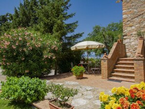 Une terrasse avec une table et des chaises en pierre, un pot de fleurs et un escalier en pierre menant à un bâtiment en pierre.