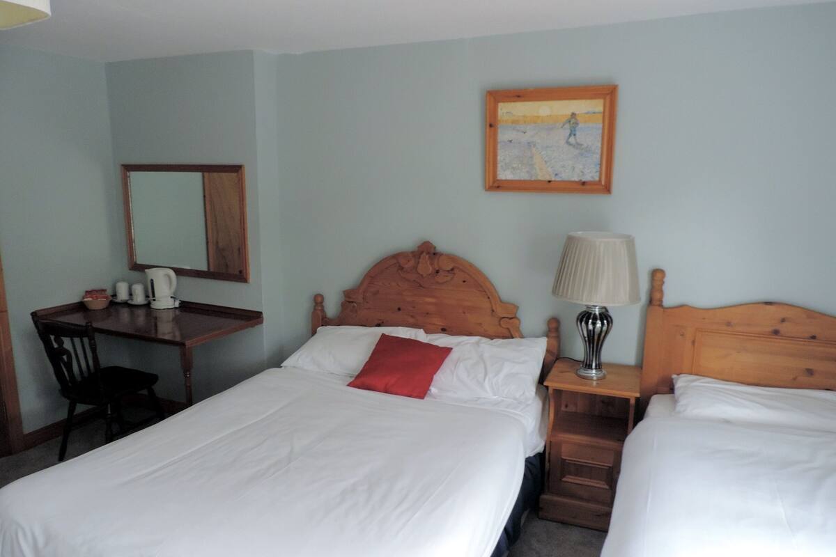 Une chambre d’hôtel avec deux lits, un bureau, une chaise, une lampe et un tableau au mur.