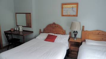 Habitación de hotel con dos camas, cabecera de madera, un escritorio con silla, una lámpara y un cuadro en la pared.