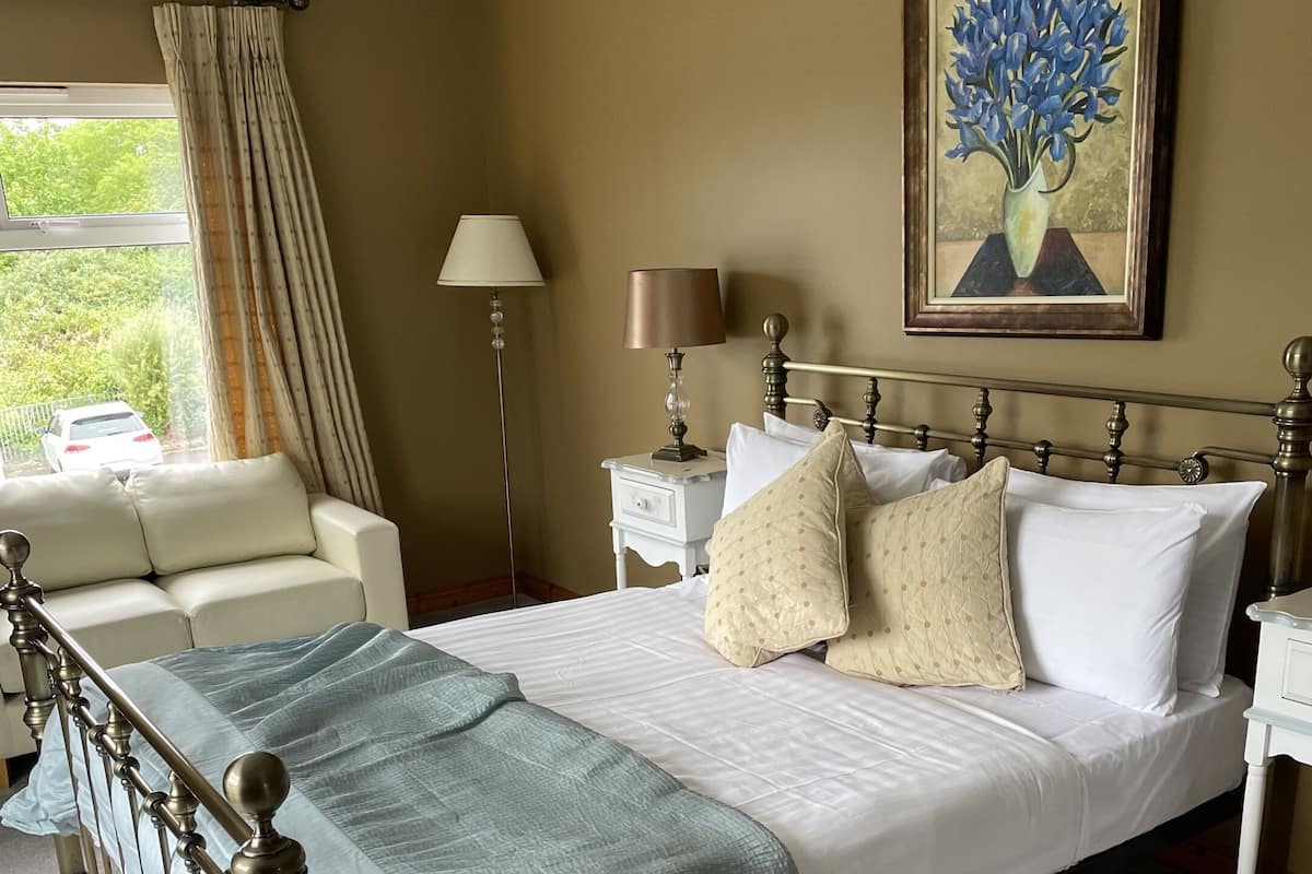 Un lit bien fait, avec une tête de lit, une table de chevet avec une lampe, une fenêtre avec des rideaux et un tableau accroché au mur.