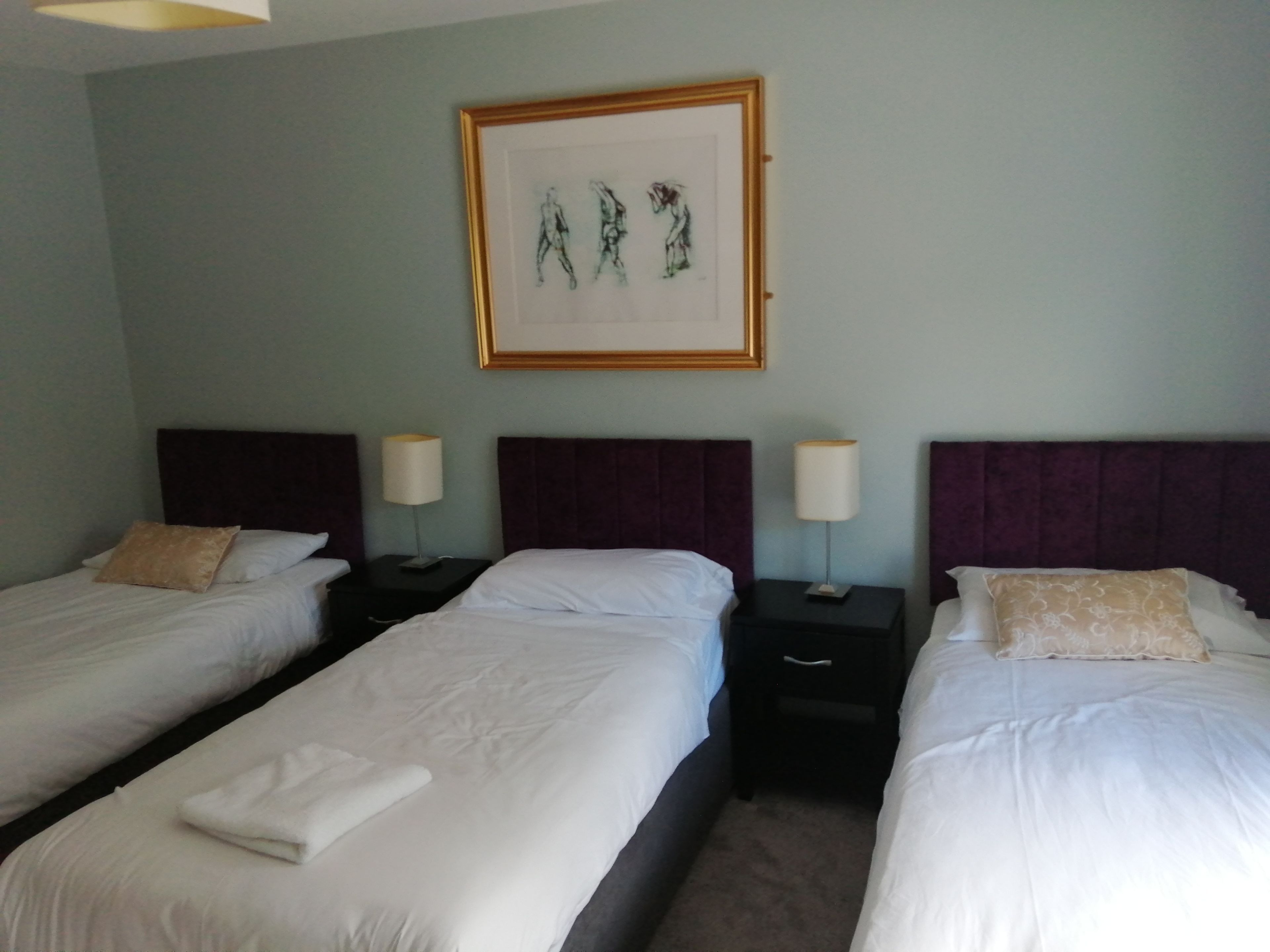 A hotel room with two single beds, each with a headboard, bedside tables, lamps, and a framed artwork above the beds.