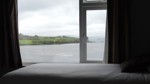 A bed with a view of a river and hills.