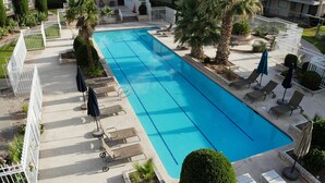 A rectangular swimming pool with clear blue water, surrounded by a white fence. There are lounge chairs and umbrellas along the poolside. - NEWLY UPGRADED Beautiful One Bedroom, One Bath, Sports Village Condo (St. George)