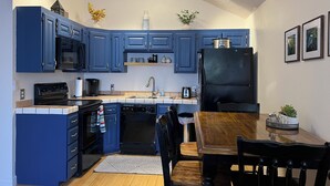 A compact kitchen with blue cabinets, a black refrigerator, and a wooden dining table with chairs. - NEWLY UPGRADED Beautiful One Bedroom, One Bath, Sports Village Condo (St. George)