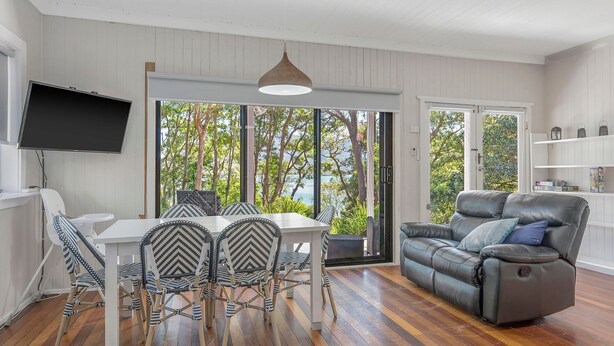 A modern living room with a dining area, a leather sofa, and a TV mounted on the wall. - Seascape - 154 Camden Head Rd Dunbogan (Dunbogan)