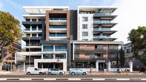 Een meerlaags gebouw met een modern architectonisch ontwerp, voorzien van balkons, grote ramen en een combinatie van materialen.