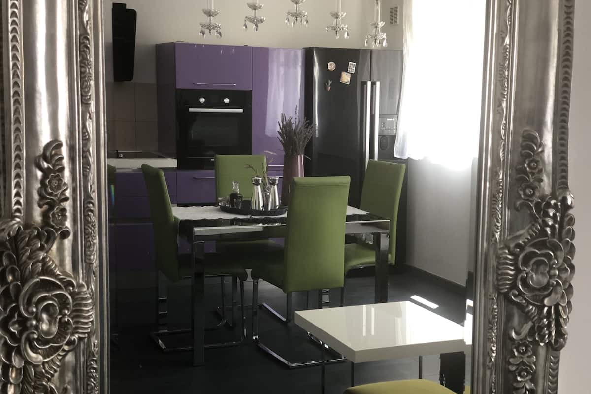 Une cuisine moderne avec un coin repas, comprenant une table blanche, des chaises vertes et un meuble violet.