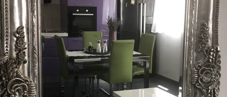 Una cuina moderna amb zona de menjador, amb taula blanca, cadires verdes i armari morat.