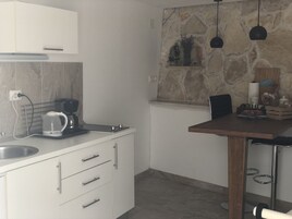 Una cocina moderna con armarios blancos, cafetera, salpicadero de piedra e iluminación colgante.