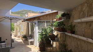 A sunlit patio with stone flooring, a white table and chairs, and various potted plants. - Casa di Lavanda (Hvar)
