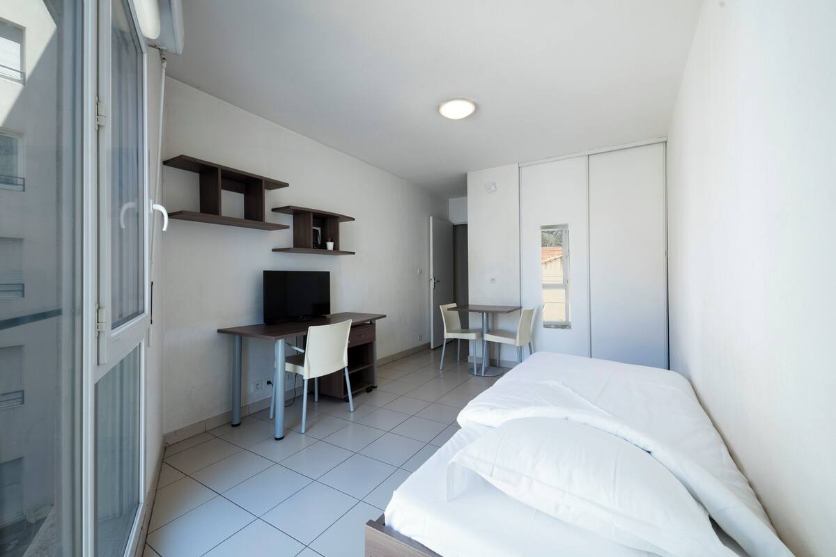 Een slaapkamer met een bed, bureau, stoel en televisie.