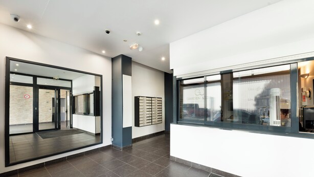 A modern lobby with a glass door entrance, a reception desk, and a large window with a city view. - Garden & City Toulon (Toulon)