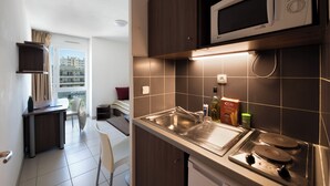 A compact kitchen with a microwave, sink, and stove. There's a dining area with a chair and a table. - Garden & City Toulon (Toulon)